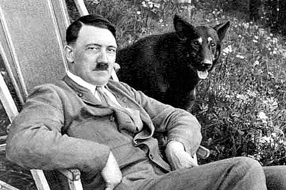 Historical black and white photograph of Adolf Hitler seated outdoors with his German Shepherd, Blondi.