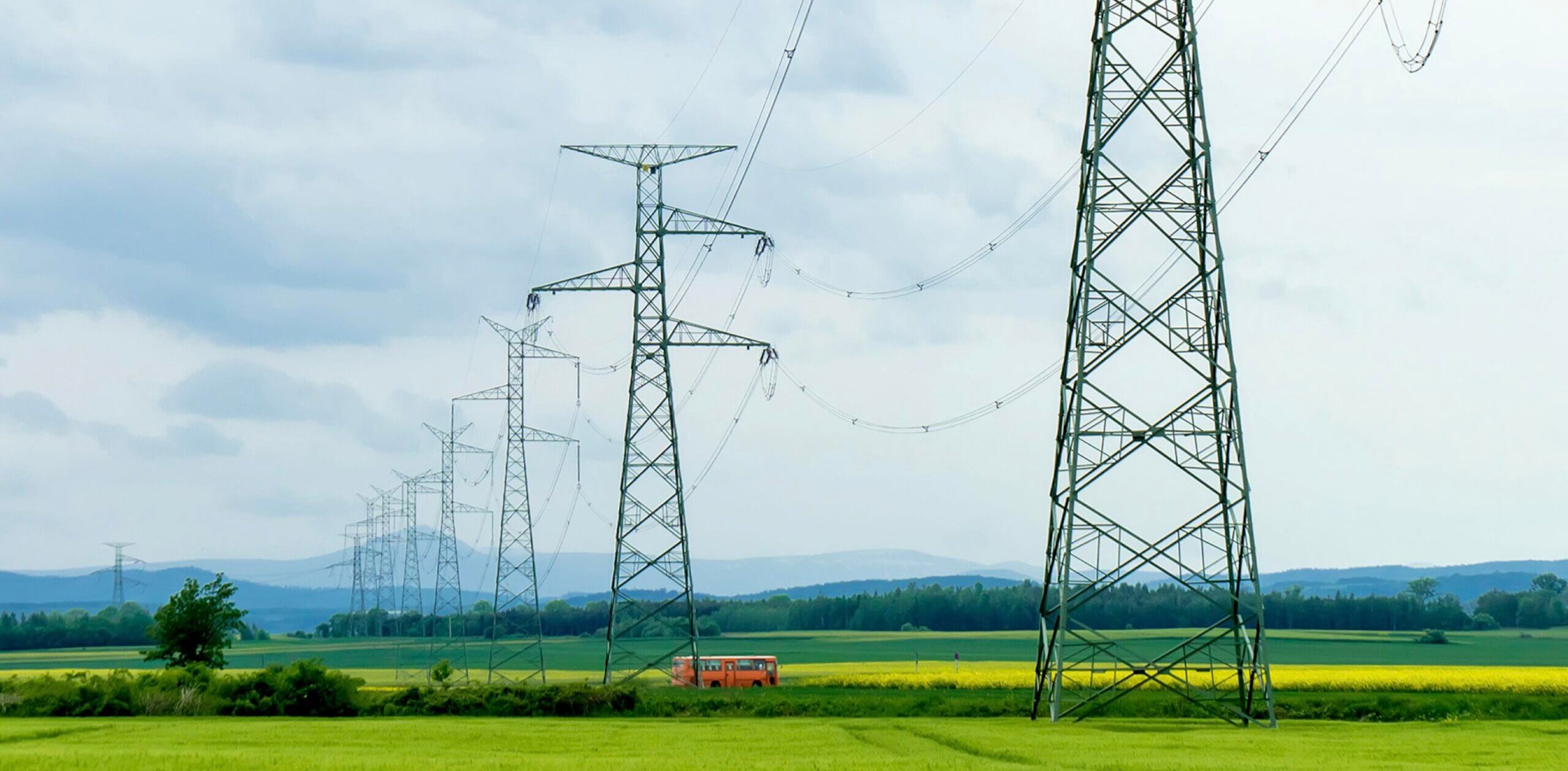 High-voltage transmission towers crossing green farmland under a cloudy sky.
