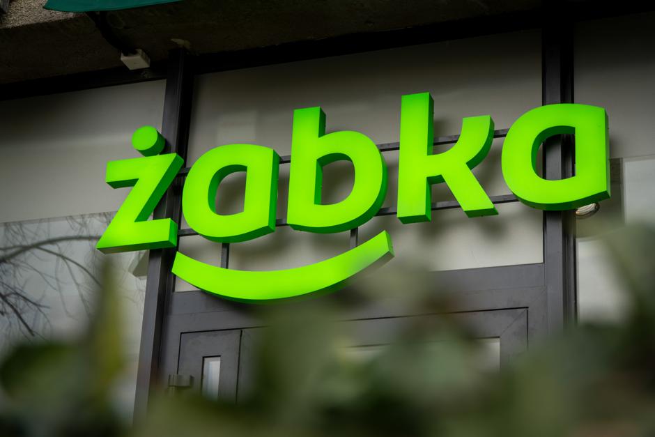 Illuminated Żabka storefront sign with the brand's green frog-smile logo.